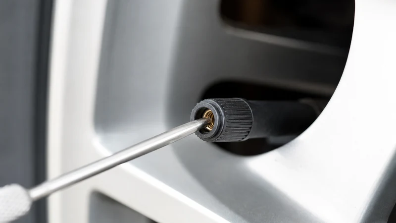 Small screwdriver or pen tip pressing the center pin of a valve stem to release air from an over-inflated tire