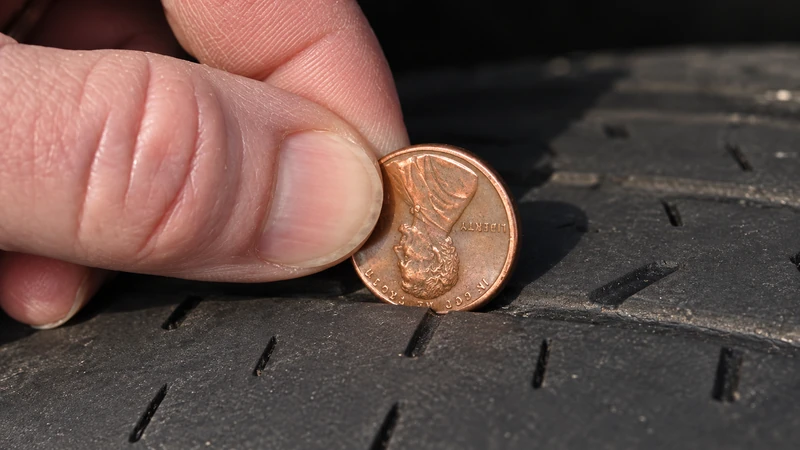 A penny standing in the groove of a worn tire with Lincoln's entire head visible above the shallow tread, showing a failed penny test