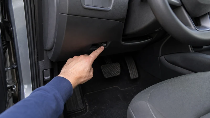 Photo of TPMS reset button location under the dashboard near the steering column, with finger pressing the small black button