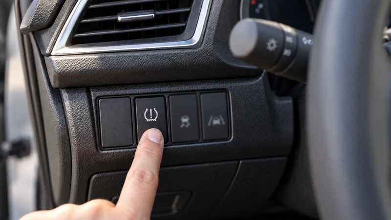 A fingertip pressing a TPMS calibration button to the left of the steering column, illustrating the procedure on equipped Honda models